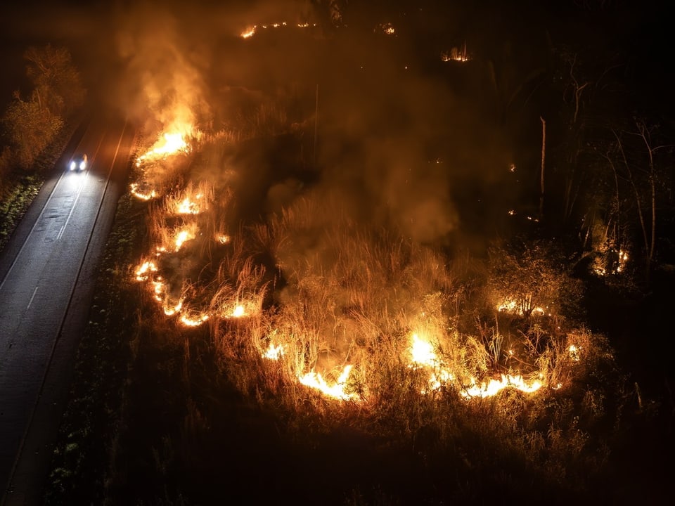 Ein Auto nehmen einem brennenden Feld in der Nacht.