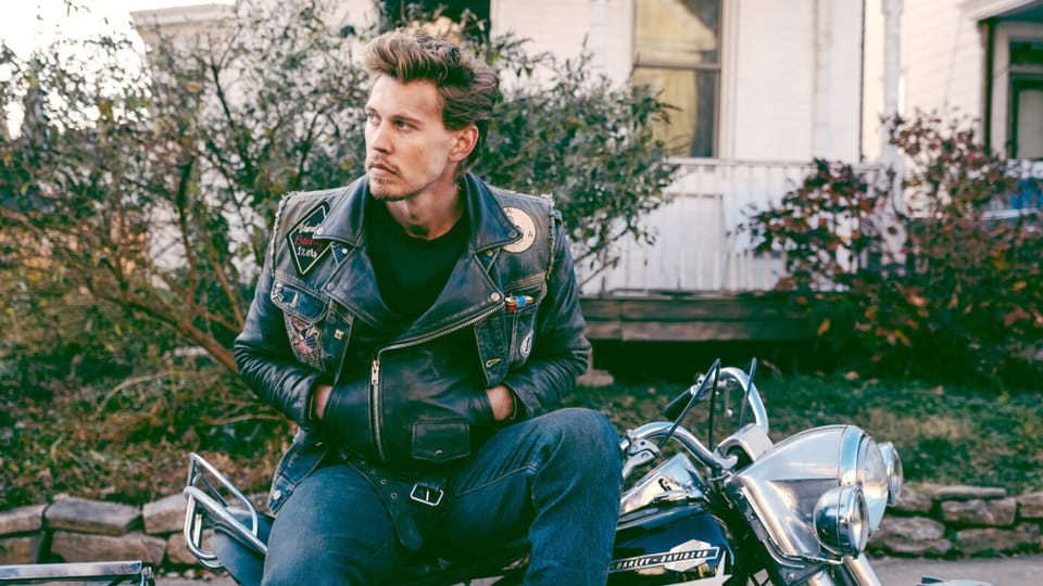 Ein Mann in Lederjacke und Jeanshose sitzt auf einem klassischen Motorrad.