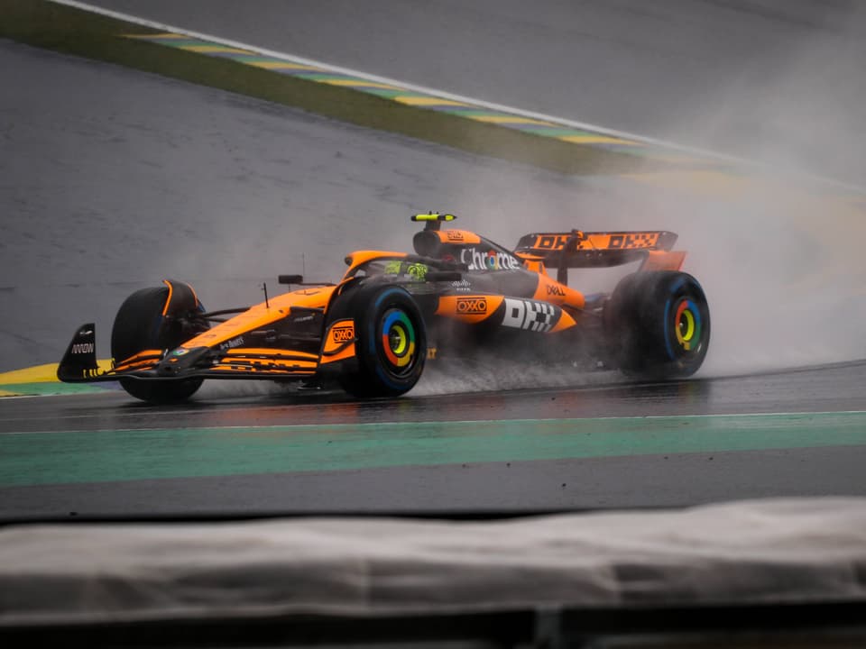 Orange Formel-1-Wagen fährt auf regennasser Strecke.