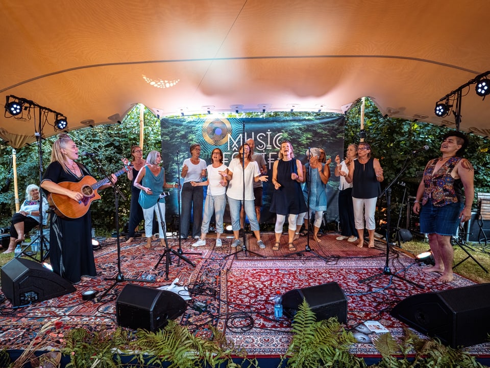 Musikgruppe singt auf beleuchteter Bühne im Freien.