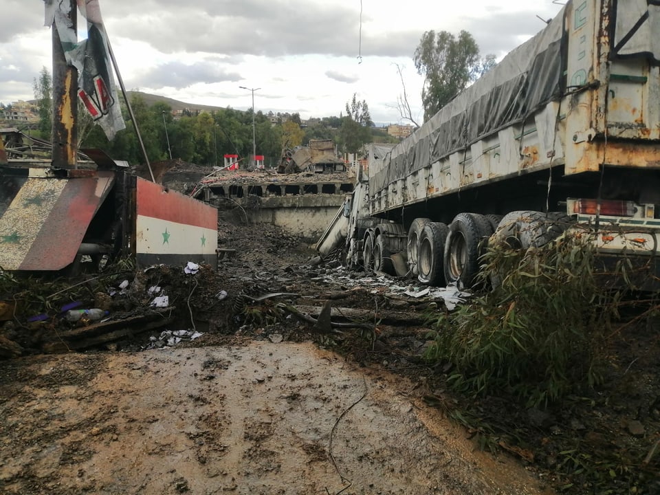 Verwüstete Szene mit einem umgestürzten Lastwagen und Trümmern auf schlammigem Boden.