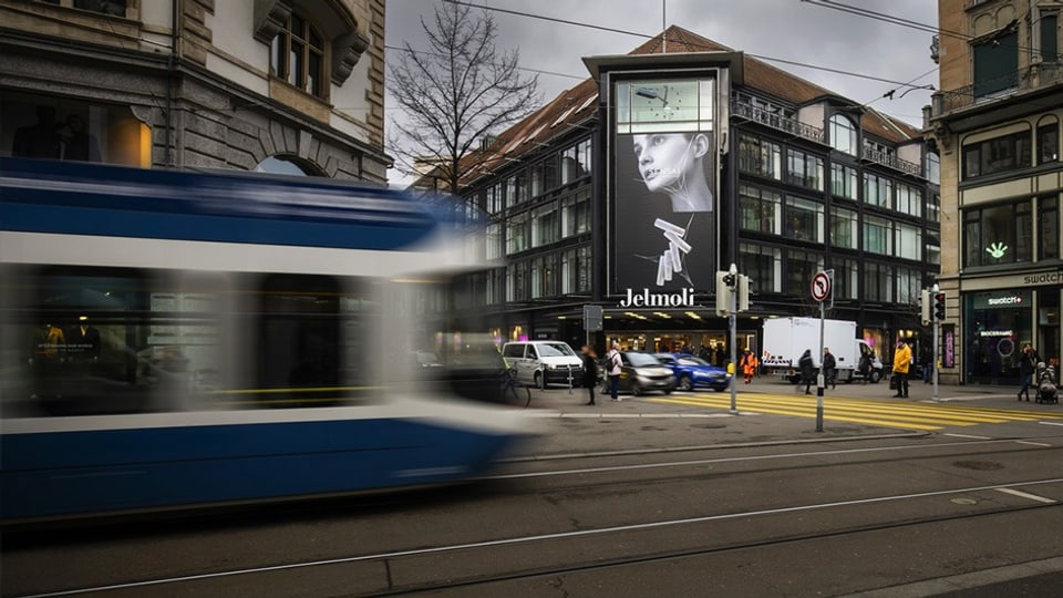 Vorbeifahrende Strassenbahn vor Gebäude mit Werbung in Stadt.