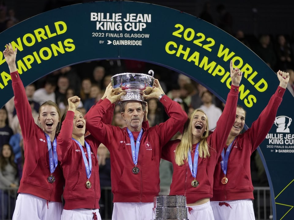 Tennisspielerinnen und Trainer feiern als Weltmeister mit Pokal.