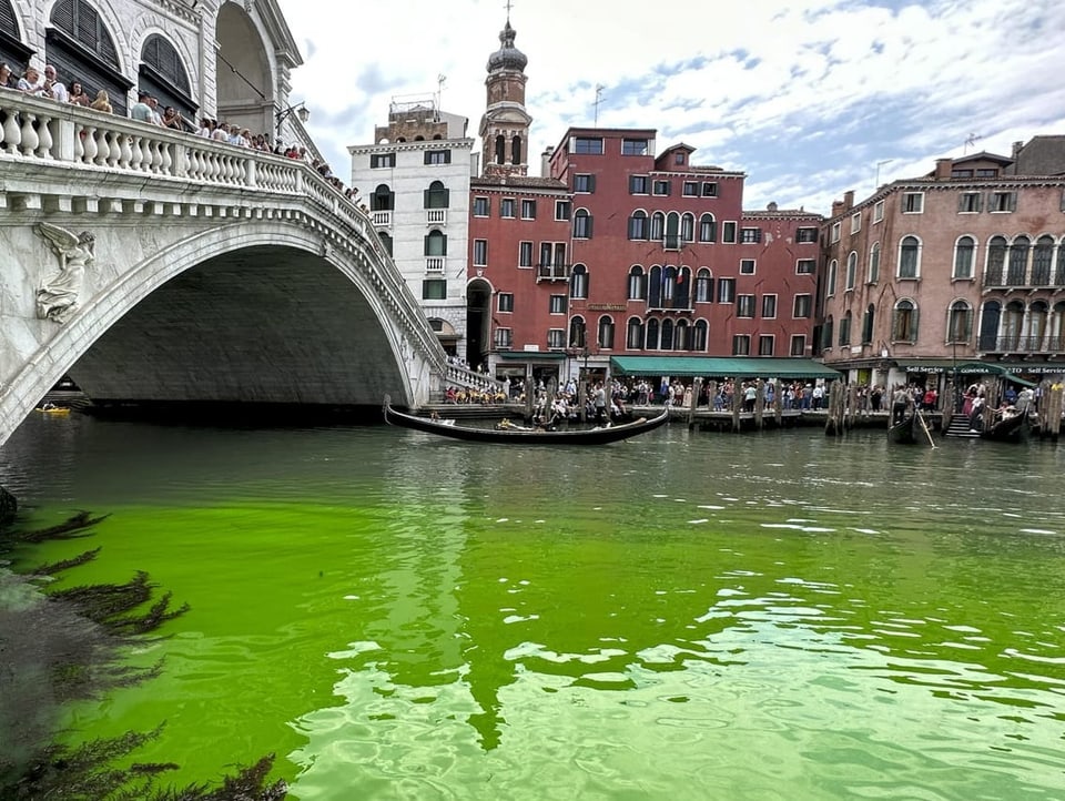 Blick auf den Canal Grande in Venedig. Eine Gondel fährt auf dem Wasser, das hellgrün leuchtet.