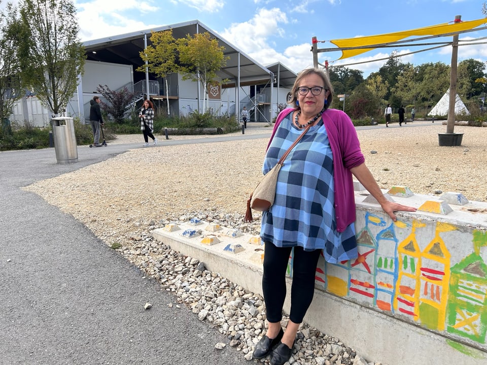 Eine Frau mit einem karierten Hemd lehnt sich gegen eine bunt bemalte Mauer. 