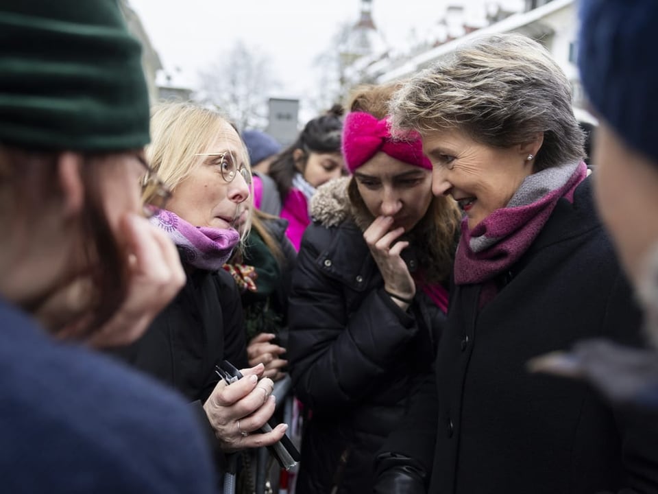 Personen unterhalten sich im Freien, tragen warme Kleidung.