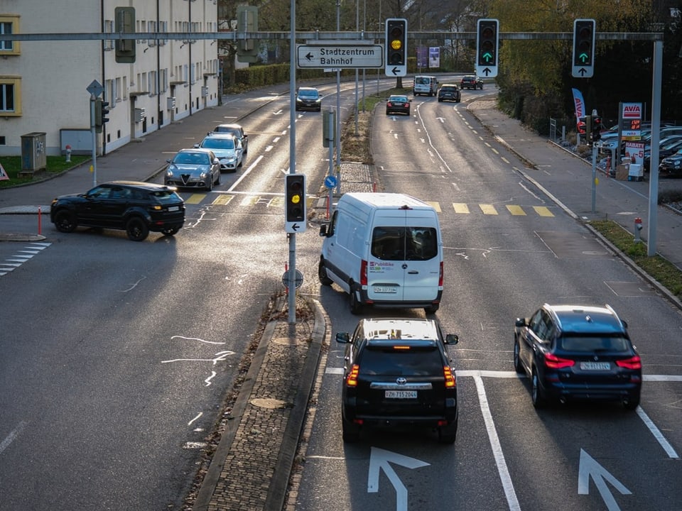 Eine vierspurige Strasse. Autos stehen an einer Ampel. 