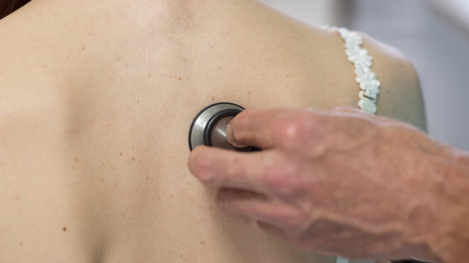 Eine Hand von einer Person im Gesundheitswesen legt ein Instrument zur Kontrolle auf einen Rücken.