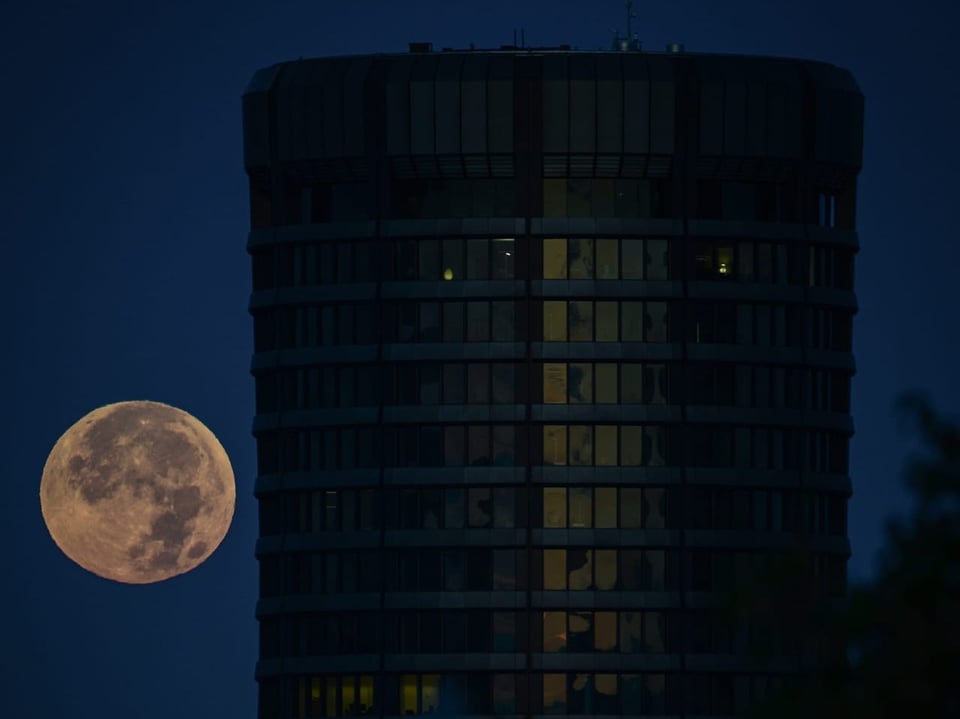 Vollmond bei Nacht neben einem Hochhaus.