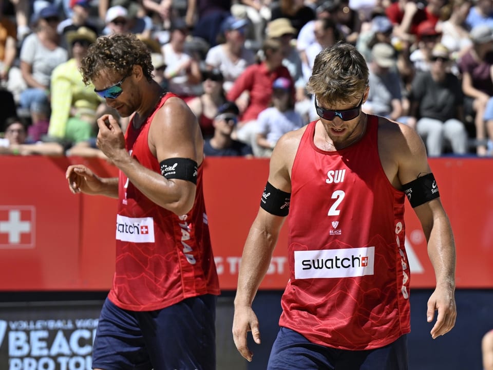 Zwei Beachvolleyballspieler in roten Trikots bei einem Turnier.