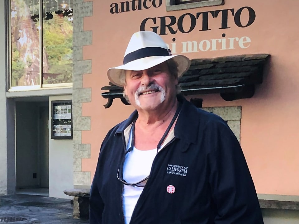 Mann in Hut vor rosa Wand des Restaurants Grotto.