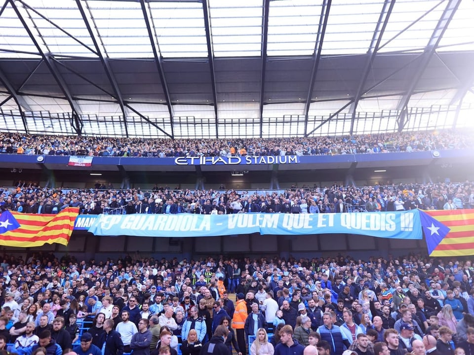 Menschenmenge im Etihad Stadium mit Transparent und Flaggen.