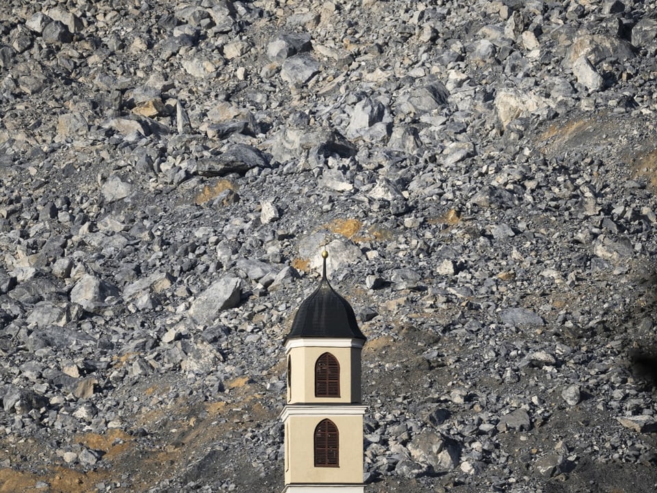 Kirchturm vor steinigem Berghang.