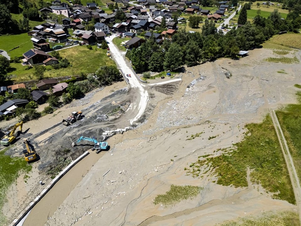 Luftaufnahme von Erdrutschgebiet mit Baggern und Dorf im Hintergrund.