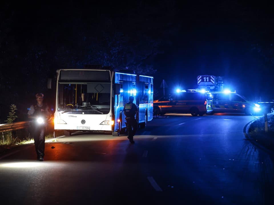 Bus und Polizeifahrzeuge mit Blaulicht bei Nacht auf einer Strasse.