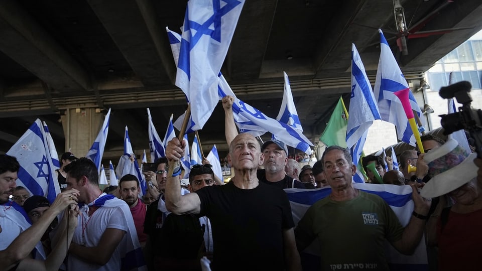 Ehud Olmert vor einer Menschenmenge, die Israel-Fahnen schwingt. Er selbst streckt auch eine in die Höhe