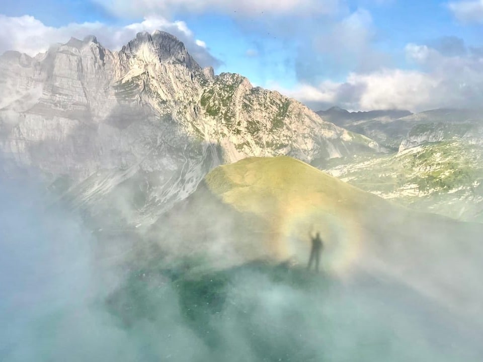 Berglandschaft im Nebel mit Schatten einer Person und Regenbogeneffekt.