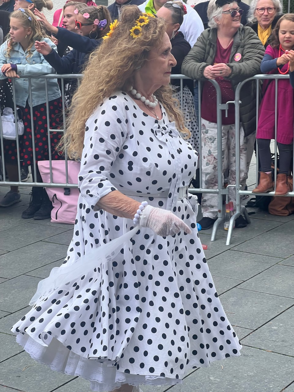 Ältere Frau im gepunkteten Kleid bei einer Veranstaltung im Freien.