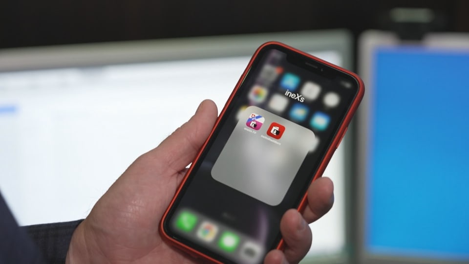Auf dem Foto hält eine Männerhand ein Handy, darauf ist ein rotes Icon für eine App zu sehen.