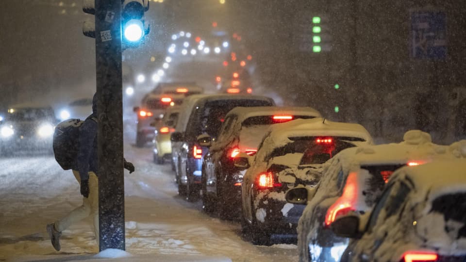 Autos im Stau bei Schneefall und grünem Ampellicht.