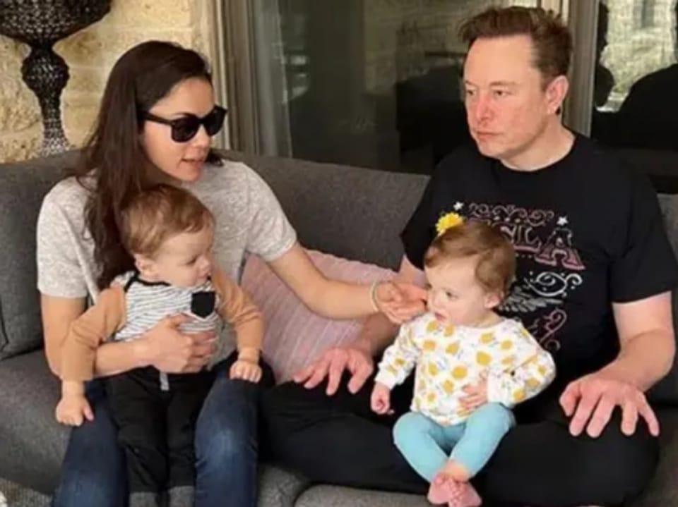 Frau mit Sonnenbrille und Mann mit schwarzem T-Shirt sitzen auf dem Sofa mit zwei Babys. 