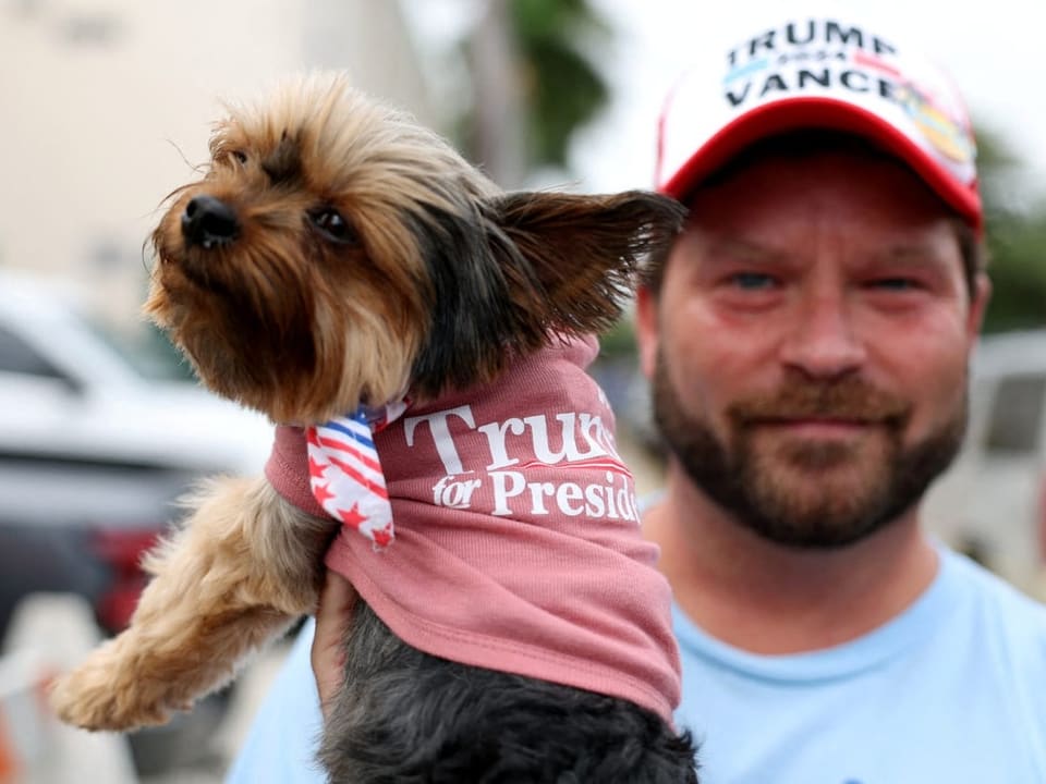 Mann hält Hund in 'Trump for President' Shirt.