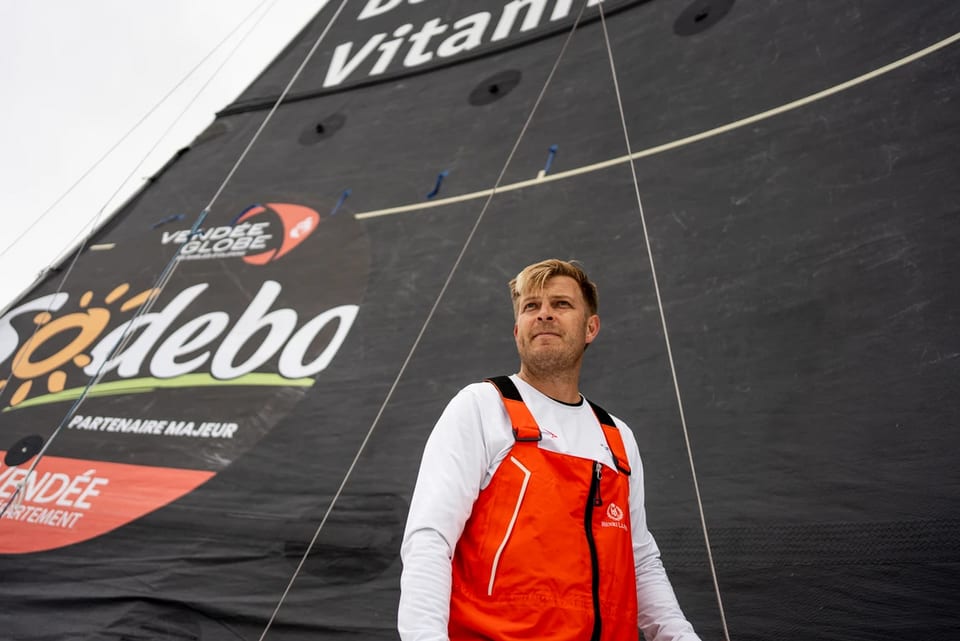 Mann in roter Segeljacke vor grossem Segel mit Logos.