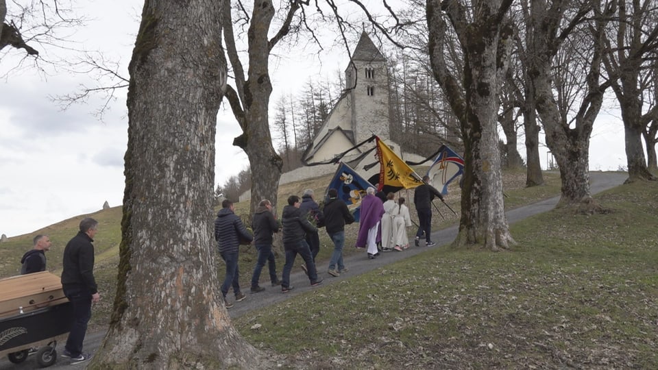 Prozession von Menschen mit Fahnen auf einem Weg zur Kirche.