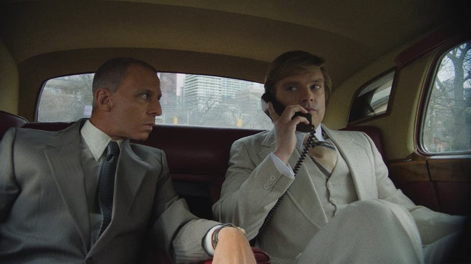Zwei Männer in Anzügen in einer Limousine, einer telefoniert.