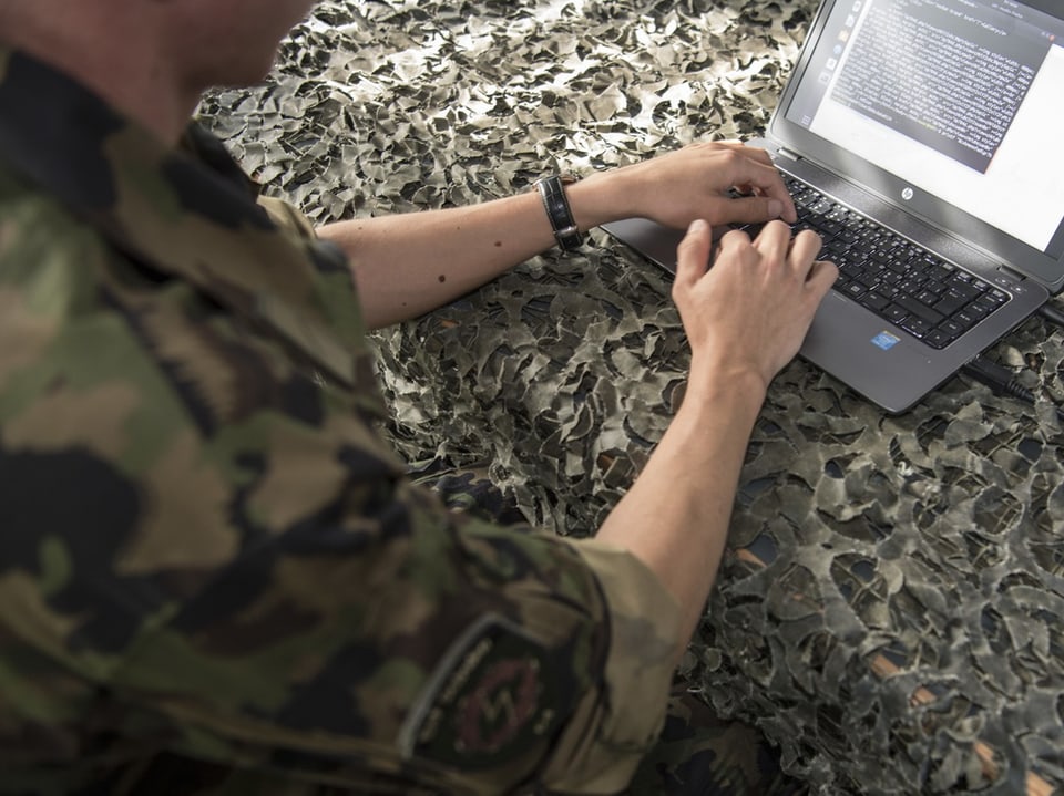 Person in Tarnuniform tippt auf einem Laptop.