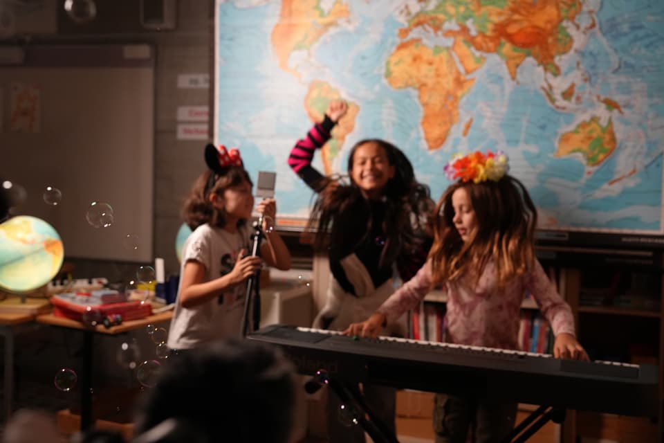 Kinder musizieren in einem Klassenzimmer mit Weltkarte im Hintergrund.