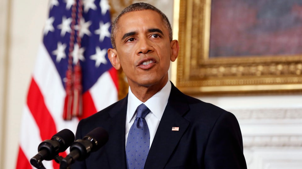 Obama spricht vor einer US-Flagge in ein Mikrofon.