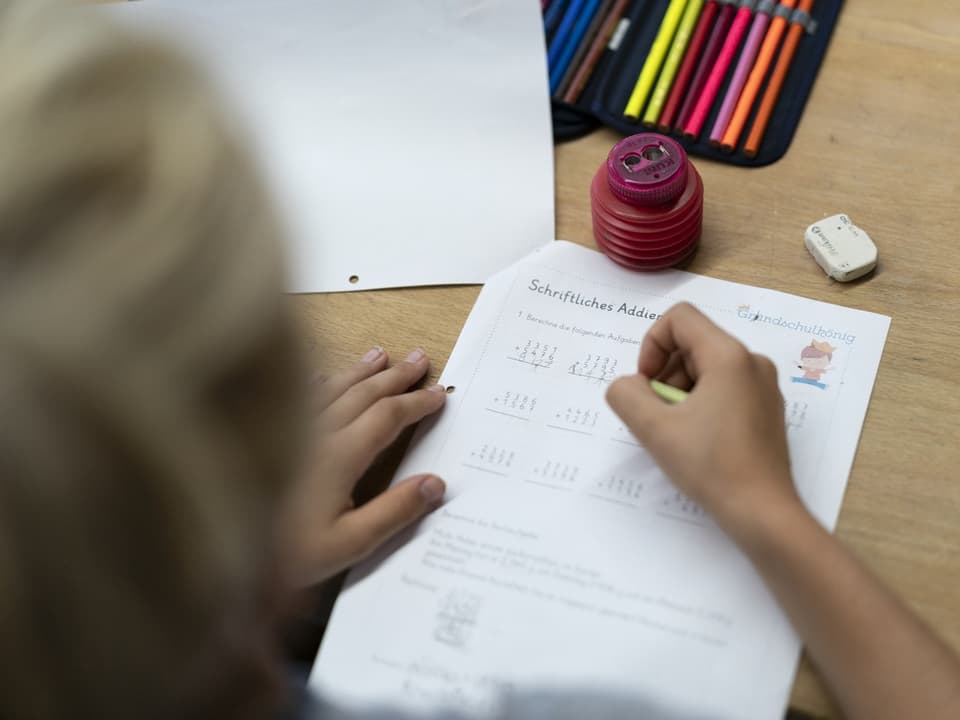 Ein Kind füllt mit einem Stift Rechenaufgaben aus. 