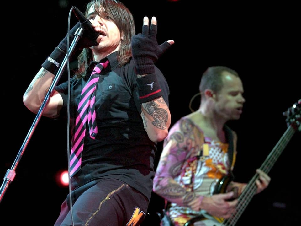 Frontsänger und Gitarrist der Red Hot Chili Peppers performen auf einer Bühne. 