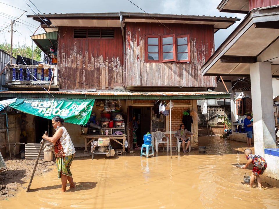 Menschen waten durch schlammiges Hochwasser vor einem Haus.