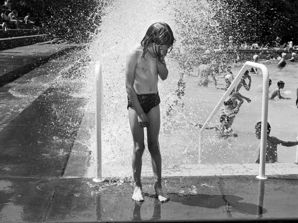 Kind unter Wassersprühgerät im Schwimmbad