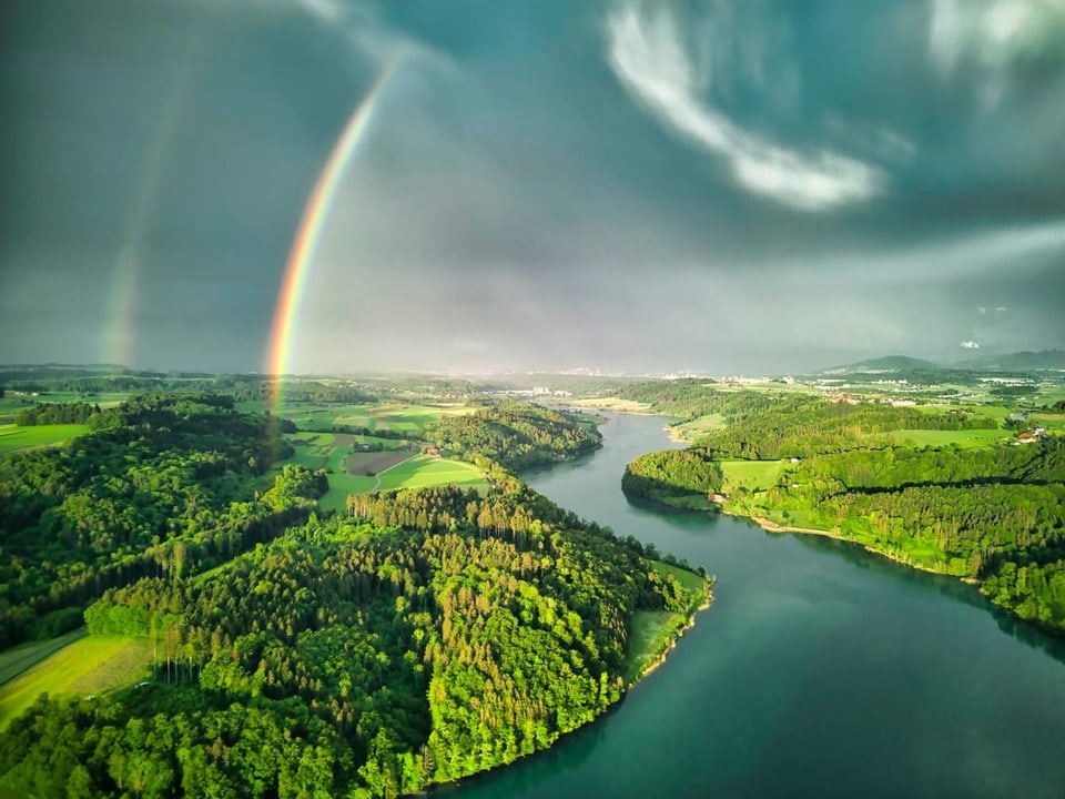 Luftaufnahme einer Landschaft mit einem doppelten Regenbogen über einem Fluss.