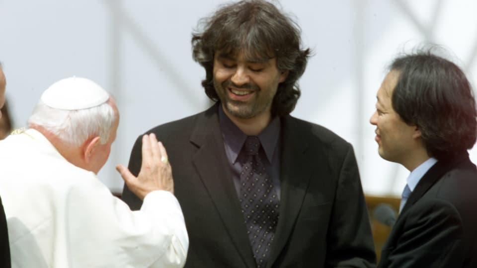 Andrea Bocelli steht vor dem Papst. Dieser trägt sein klassisch weisses Gewand während Bocelli einen schwarzen Anzug anhat. 