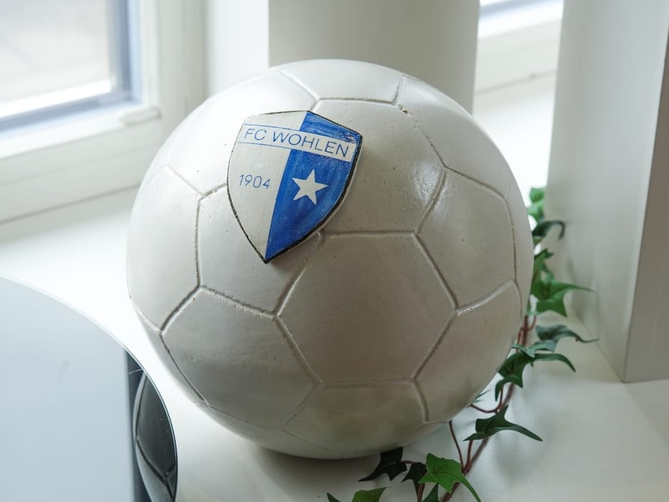 Eine Urne in Form eines Fussballs mit dem Wappen eines Fussballclubs darauf. 