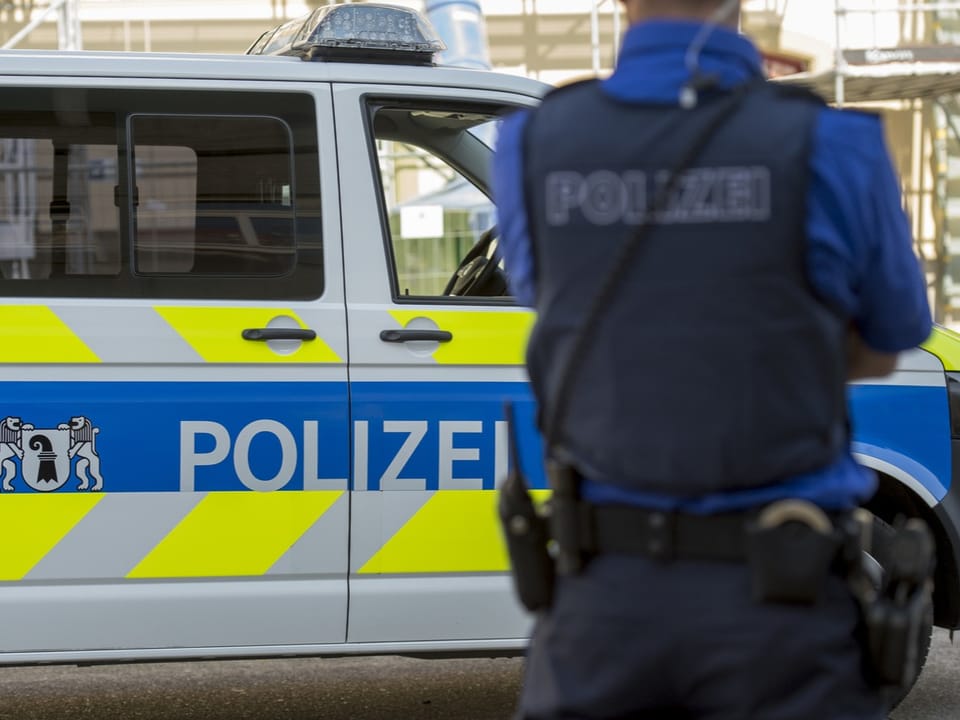 Ein Polizist steht vor einem Basler Polizeiauto.