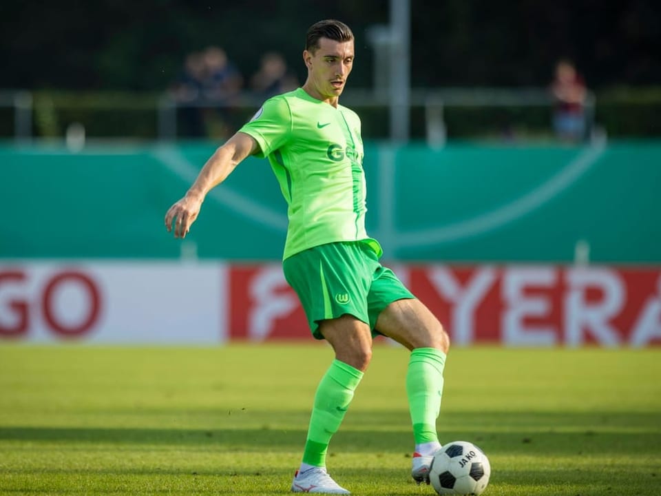 Fussballspieler in grünem Trikot am Ball auf dem Spielfeld.