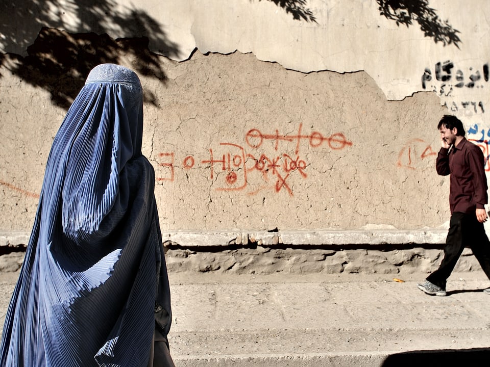 Verschleierte Frau und gehender Mann vor einer Wand mit Graffiti.