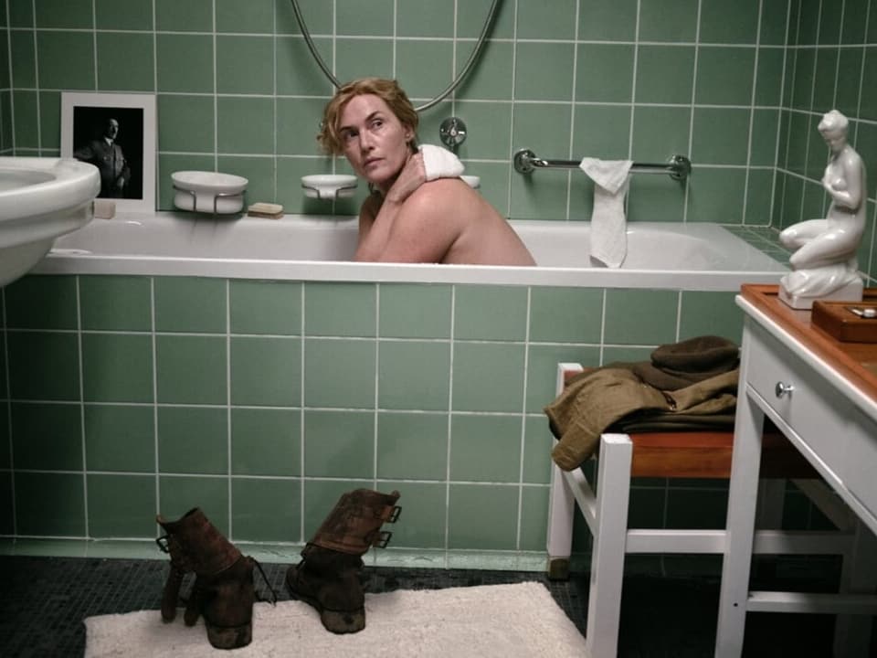 Woman in bathtub in green tiled bathroom.