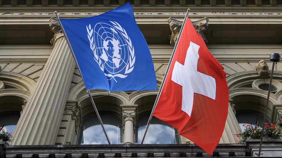 Flagge der UNO und der Schweiz an der Fassade des Bundeshauses.