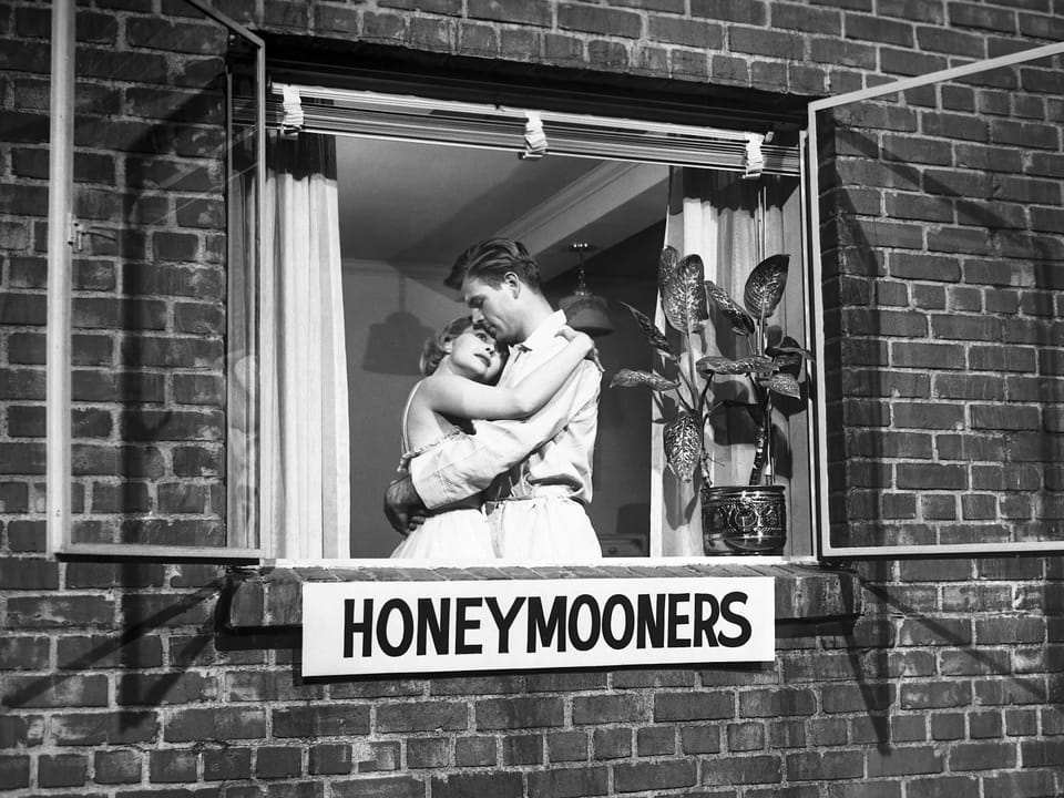 Paar umarmt sich im Fenster eines Backsteinhauses mit einem Honeymooners-Schild.