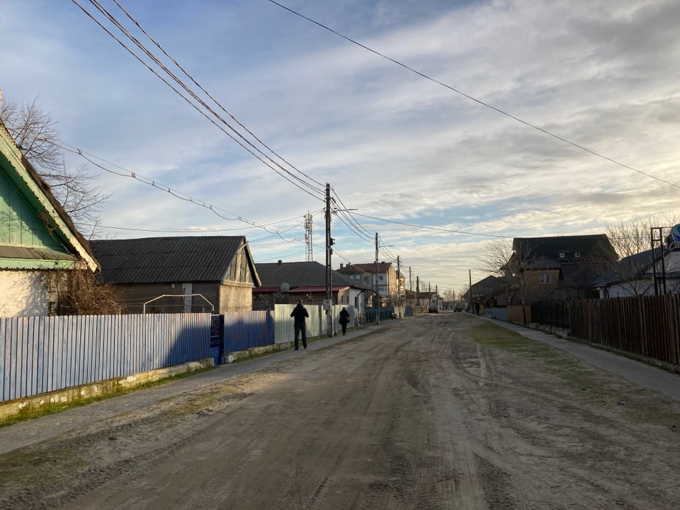 Schotterstrasse in einem Dorf mit Häusern und Stromleitungen.