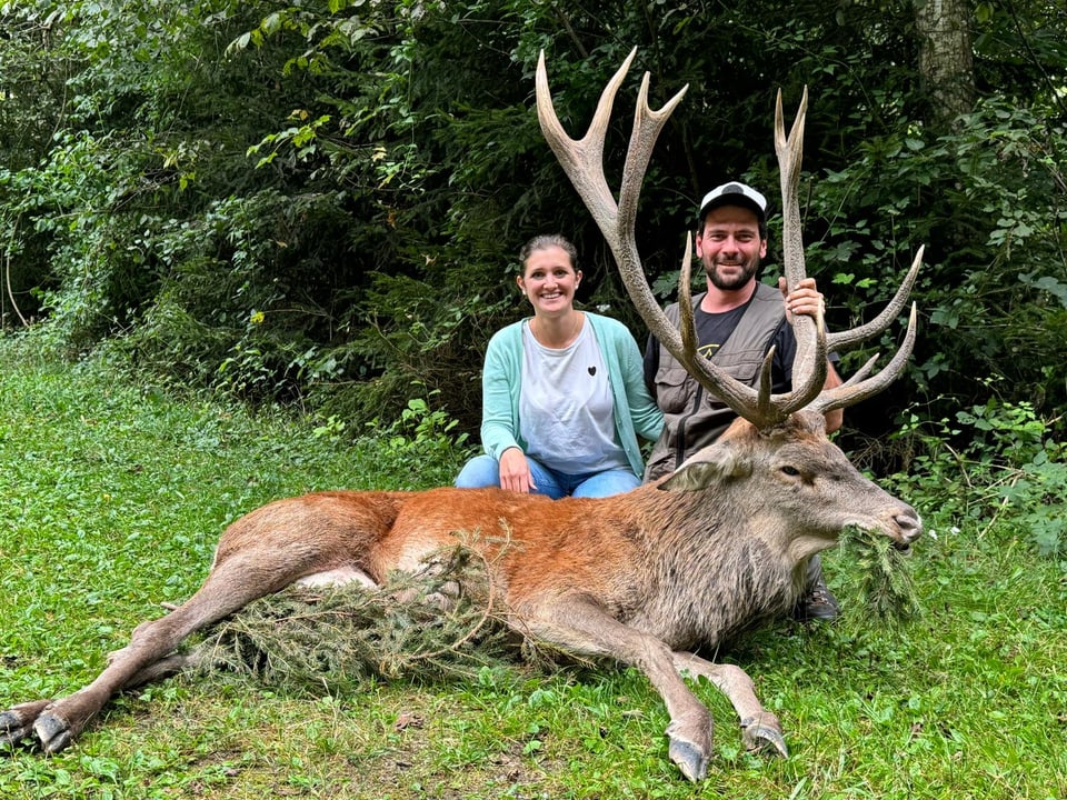 Zwei Personen posieren mit einem erlegten Hirsch im Wald.