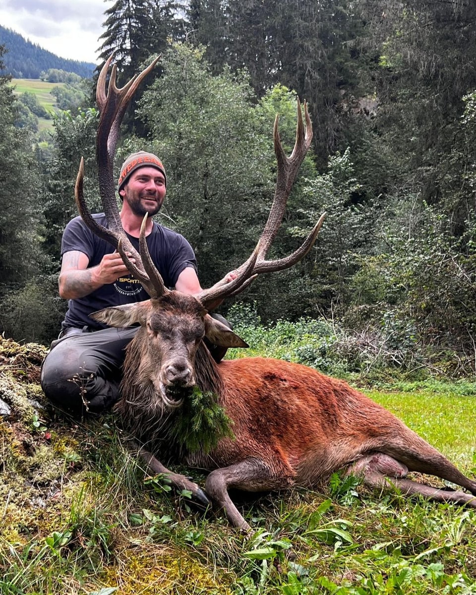 Mann posiert mit erlegtem Hirsch im Wald.