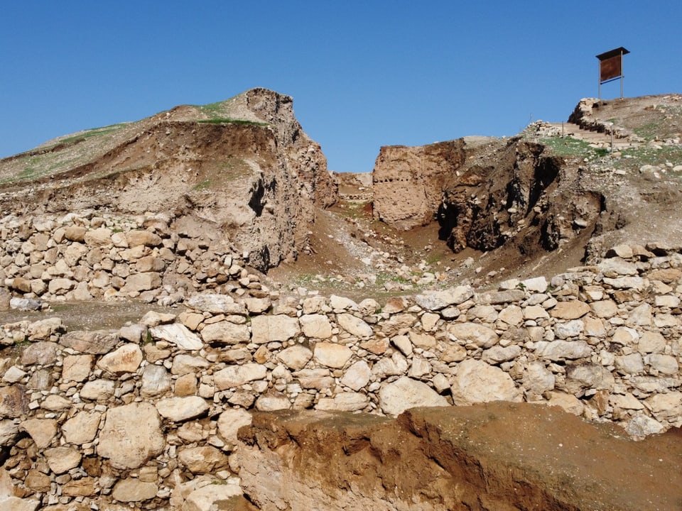 Ruinen einer archäologischen Grabungsstätte. Viele Steine und Felsen vor blauem Himmel.