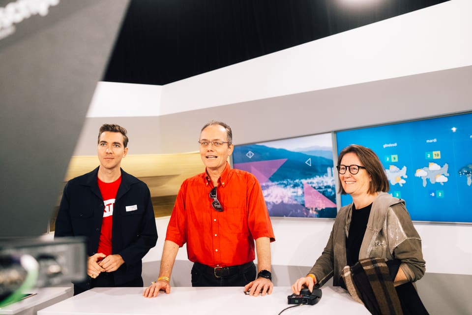 Drei Personen im Fernsehstudio vor Bildschirmen stehend.